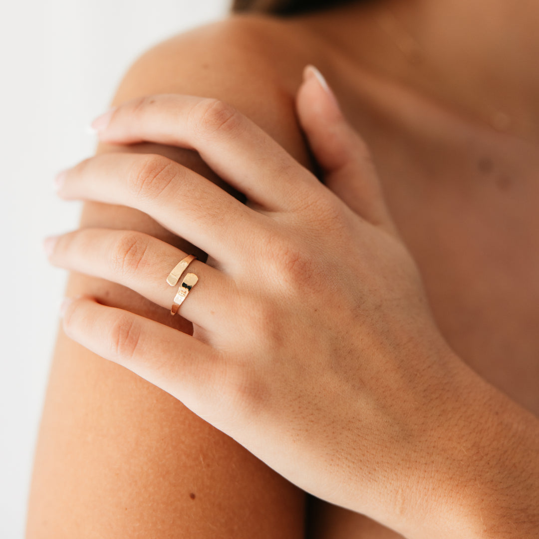 Close-up of a hand wearing a gold adjustable wrap ring on a neutral background