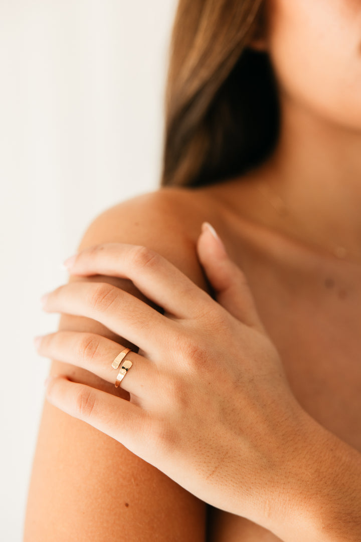 Close-up of a person wearing a gold adjustable wrap ring on a neutral background