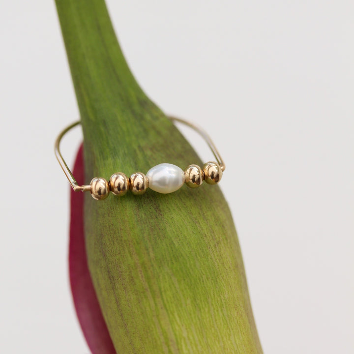 Close-up of the Beaded Pearl Remi ring, a freshwater pearl set between 14k gold filled beads, resting on a green calla lily stem