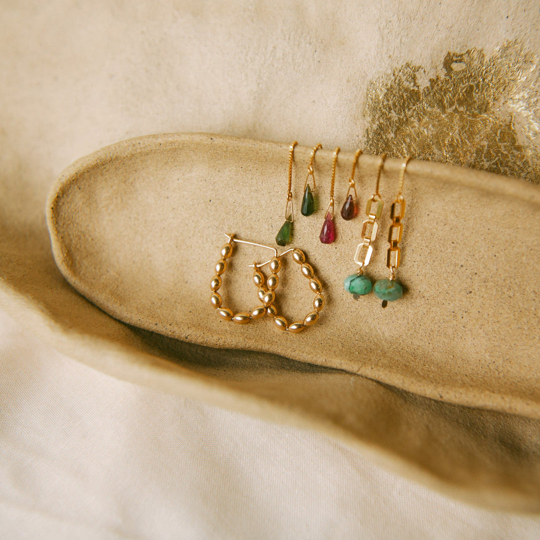 Solace Hoops handmade jewelry in gold with various colorful accent earrings displayed on a soft surface