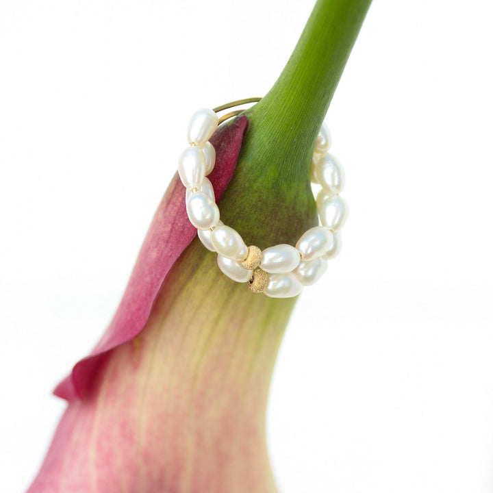 Pearl Solace hoop earrings hanging from a pink calla lily stem