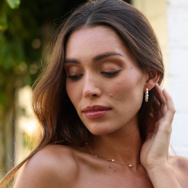 Model looking down wearing Pearl Solace hoops with the Stella pearl station necklace