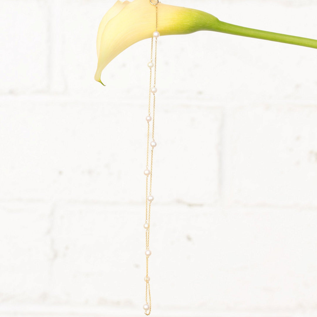 Stella necklace of freshwater pearls stationed along fine 14k gold filled chain, hanging from a cream calla lily