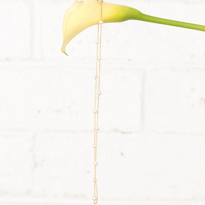 Stella necklace of freshwater pearls stationed along fine 14k gold filled chain, hanging from a cream calla lily