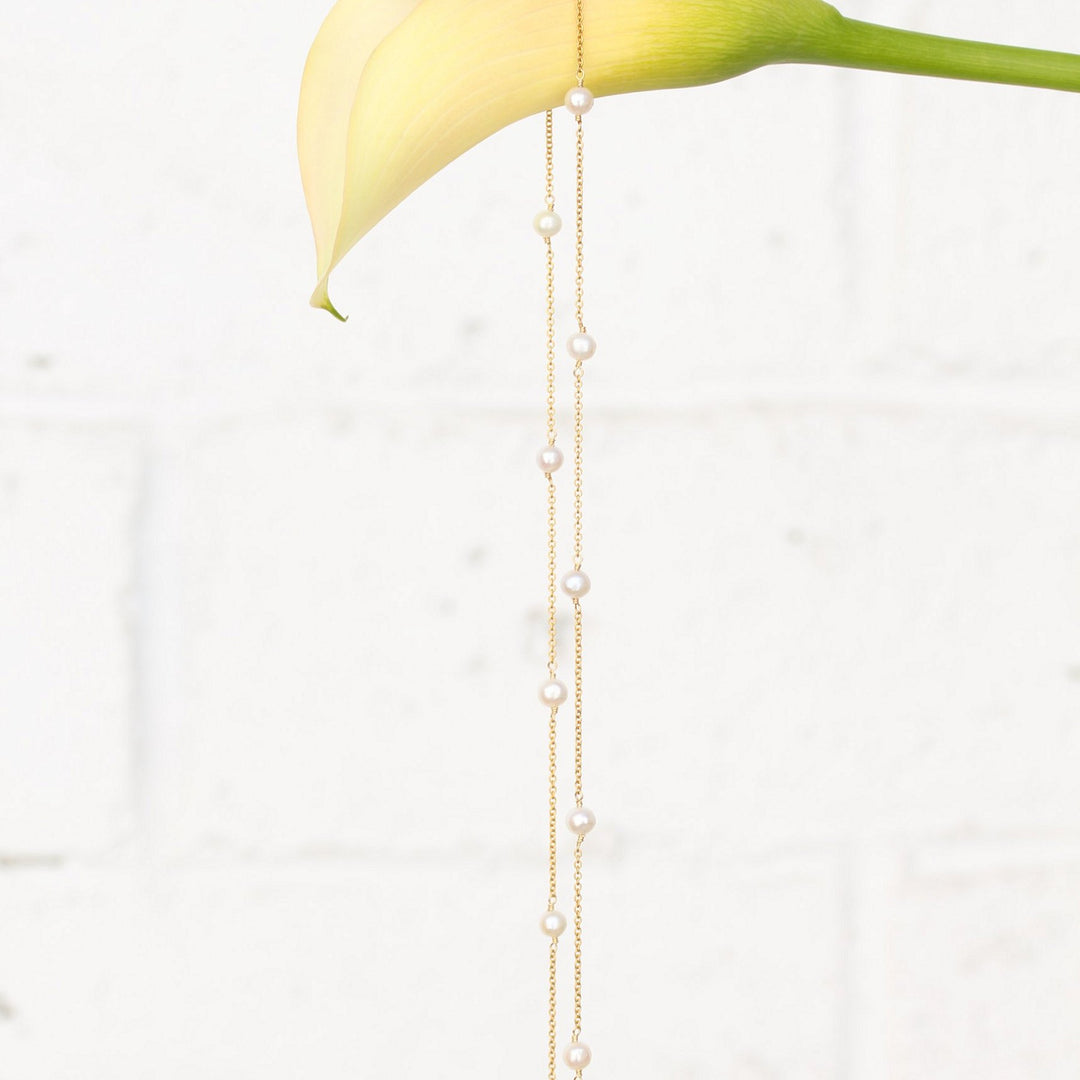 Stella pearl station necklace hanging in a long loop from a calla lily