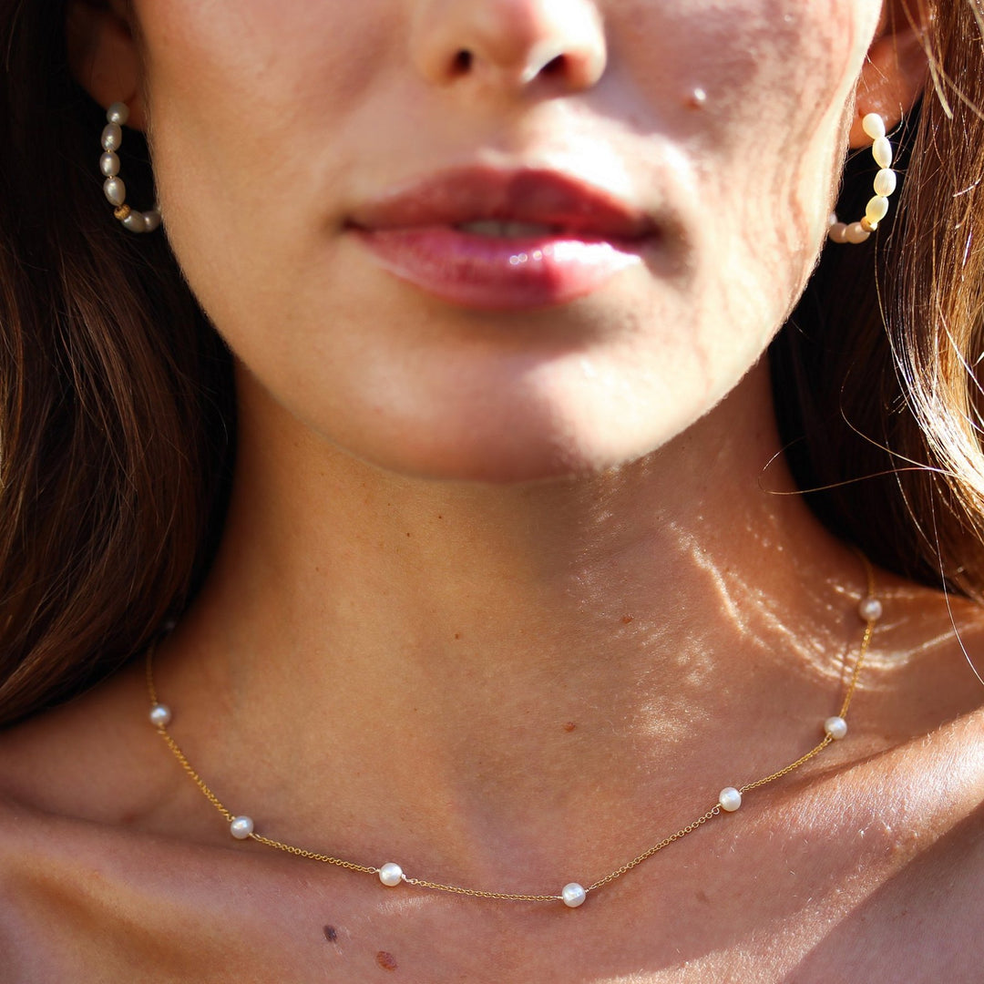 Close-up of the Stella pearl station necklace on the collarbone with pearl hoop earrings