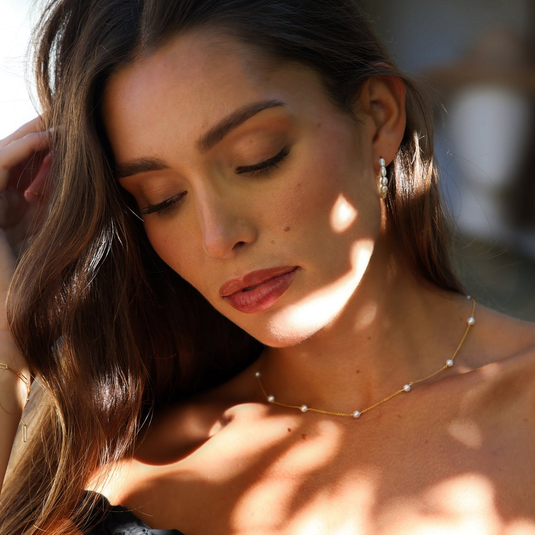 Model looking down in dappled light wearing the Stella freshwater pearl station necklace