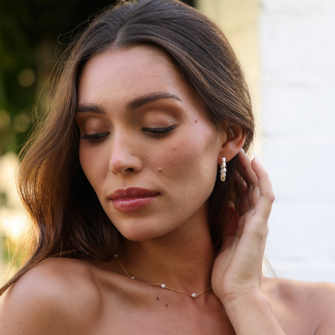 Stella pearl station necklace worn with pearl hoop earrings, hand tucked behind the ear