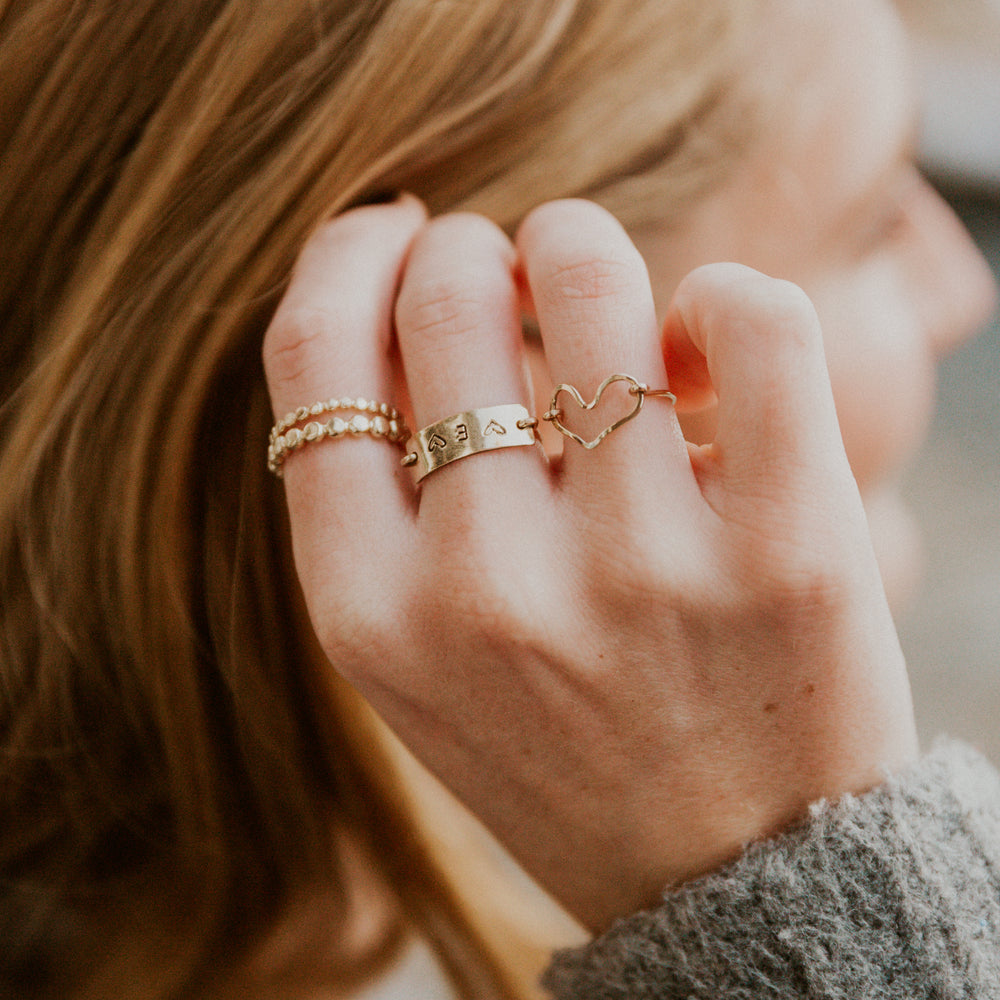 Close-up of a hand wearing multiple hand stamped personalized gold rings with a blurred background