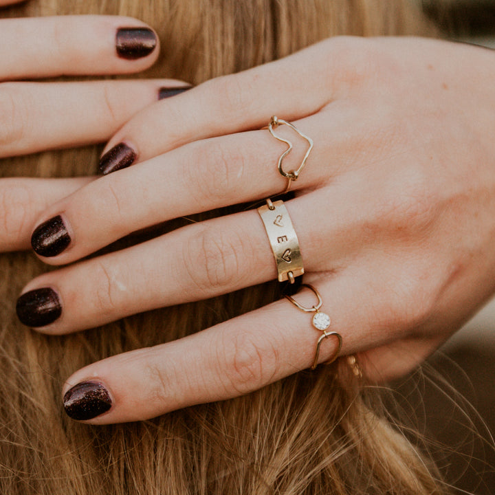 Close-up of a hand wearing gold personalized hand stamped rings with a blurred background