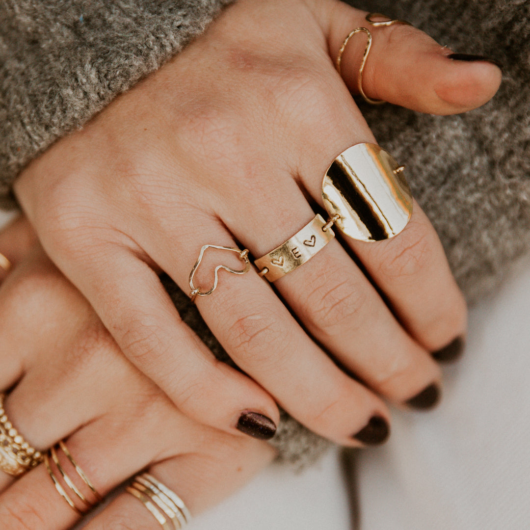 Close-up of hands wearing personalized hand stamped gold rings on a neutral background