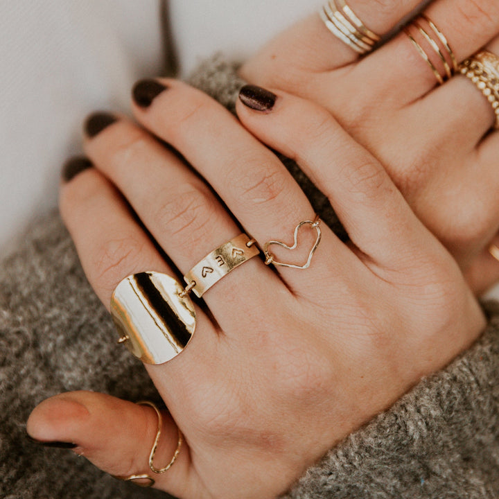 Close-up of hands wearing multiple gold rings on a neutral background
