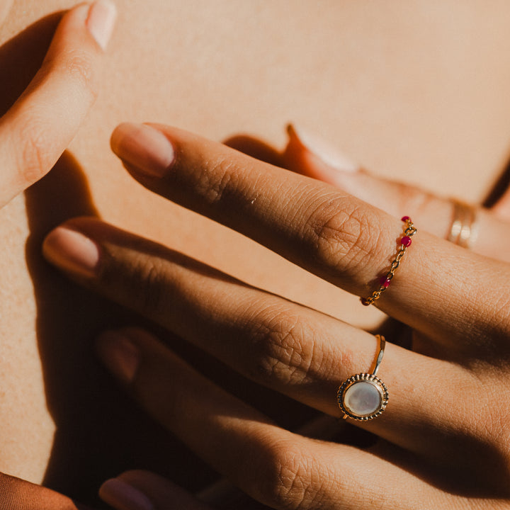 Close-up of hand with gold chain pink beaded rings on a warm-toned background