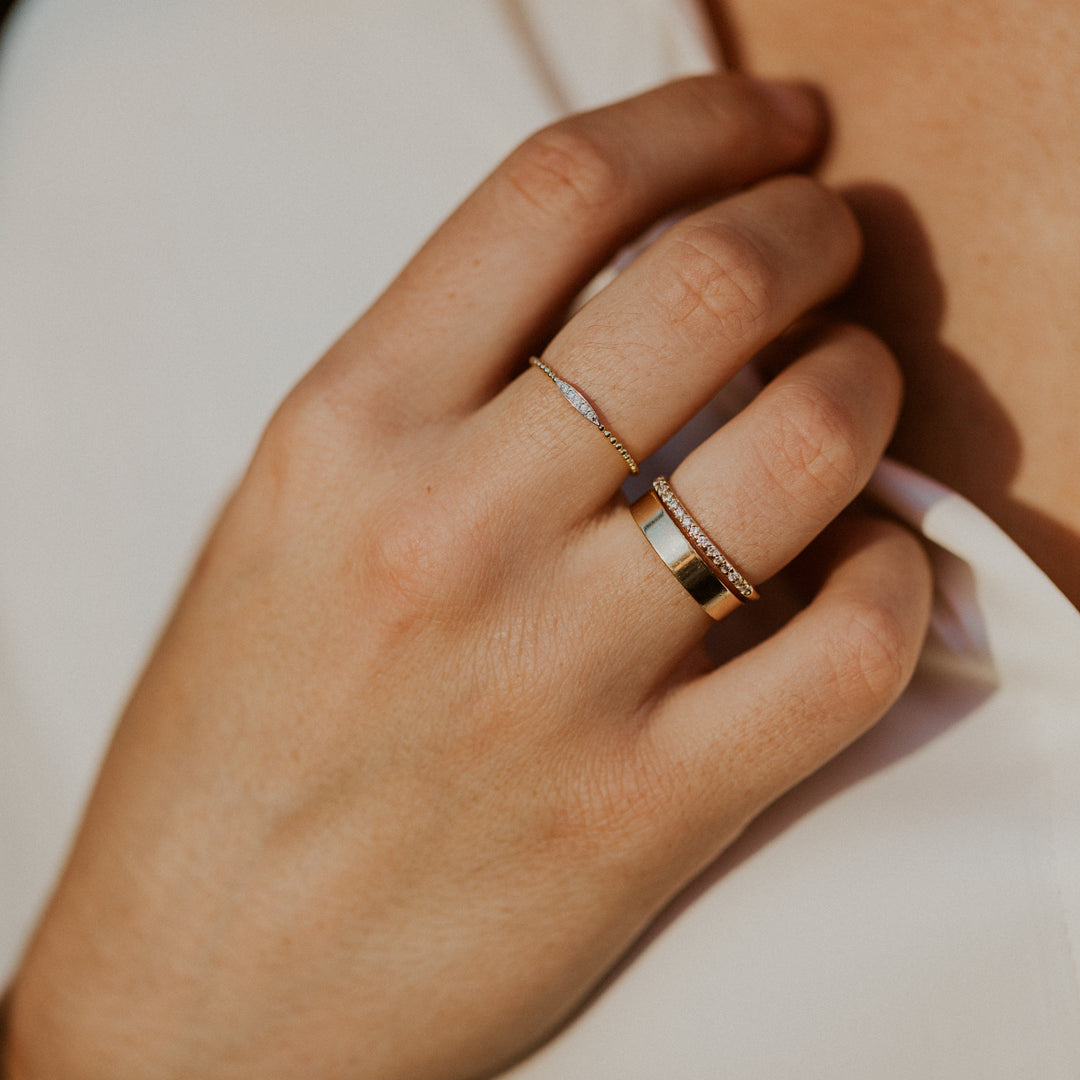 Close-up of a hand wearing two gold rings  with diamonds in an oval design on gold band