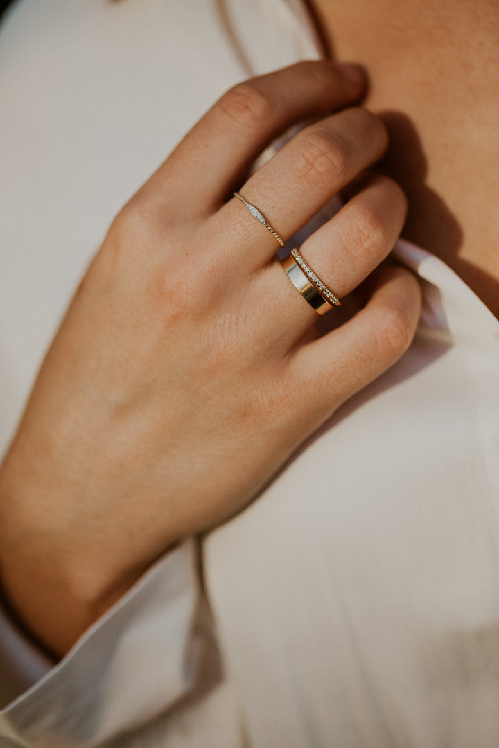 Close-up of a hand wearing two gold rings with and oval shaped design filled with diamonds