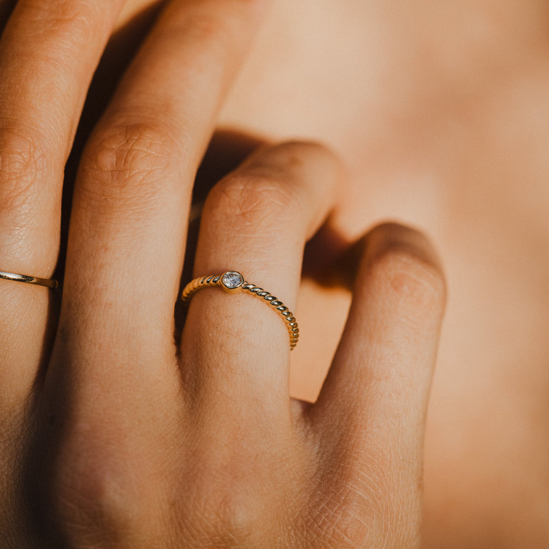 Close-up of a hand wearing 14k gold diamond rings with a warm, soft focus background.