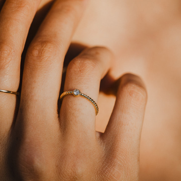 Close-up of a hand wearing 14k gold diamond rings with a warm, soft focus background.