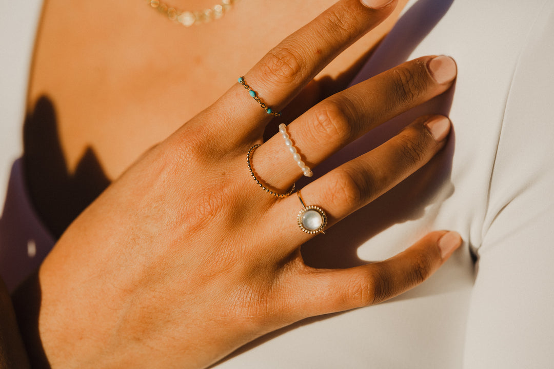Hand wearing gold chain turquoise beaded rings with a soft focus background