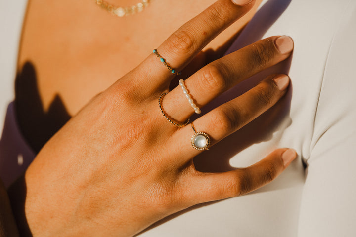Hand wearing gold chain turquoise beaded rings with a soft focus background