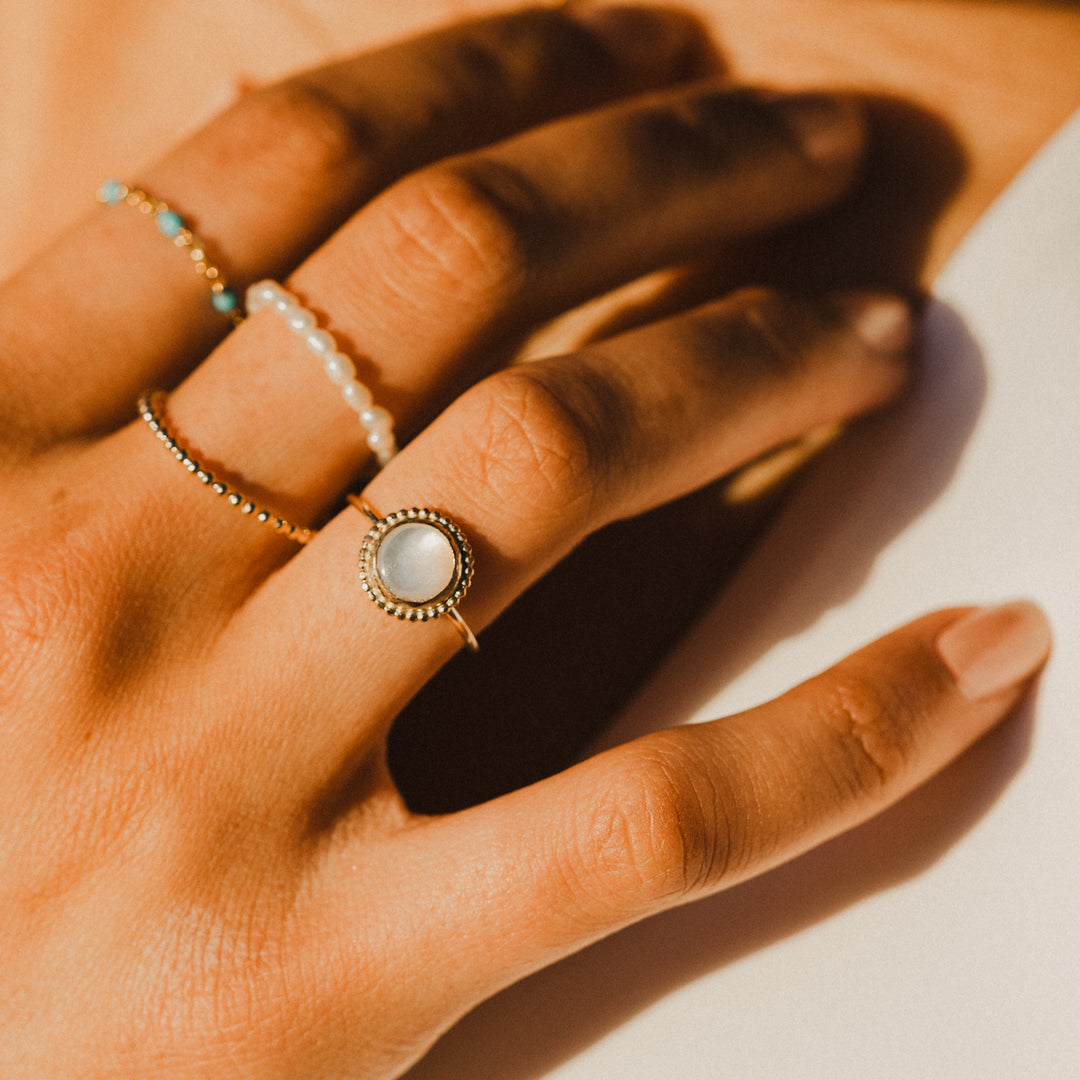 Hand wearing multiple rings with a focus on one ring with mother of pearl gemstone in gold setting