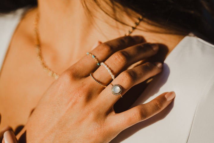 Close-up of a hand with multiple gold rings with a mother of pearl gemstone on a blurred background