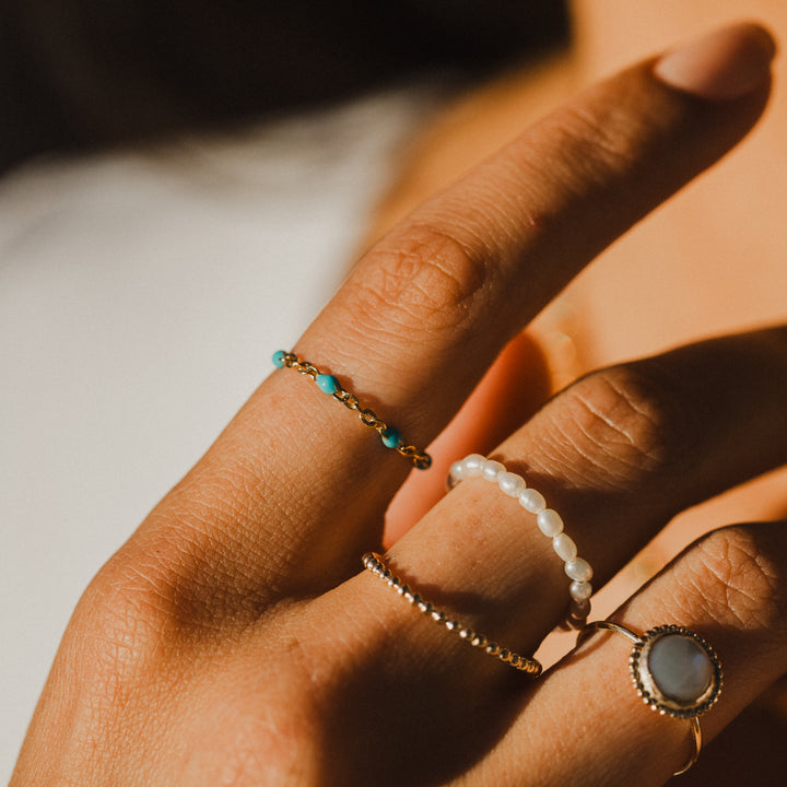 Close-up of a hand wearing gold chain turquoise beaded rings with a soft focus background