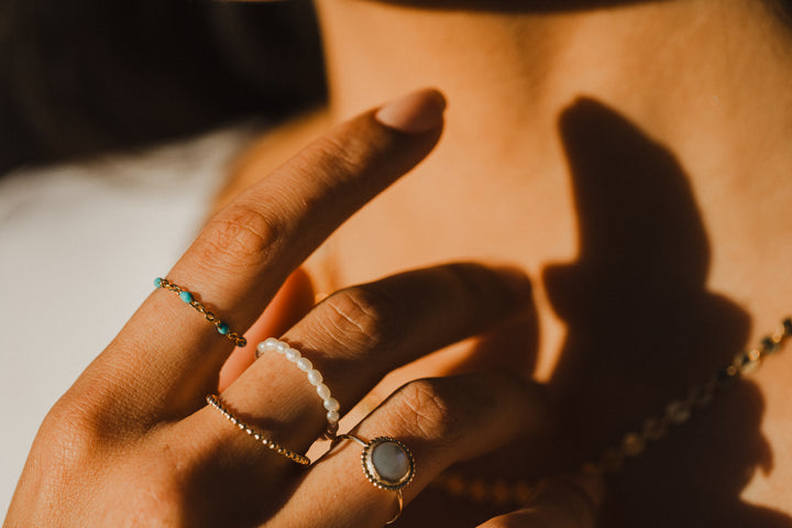 Close-up of a hand wearing gold chain turquoise beaded rings with a warm, sunlit background.