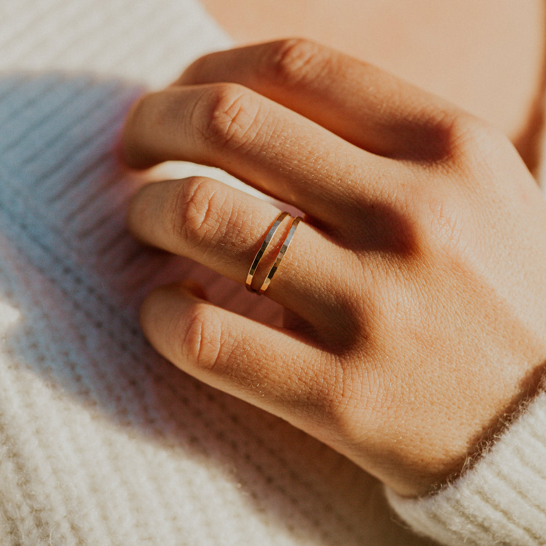 Close-up of a hand wearing a gold double wrap ring with a blurred background
