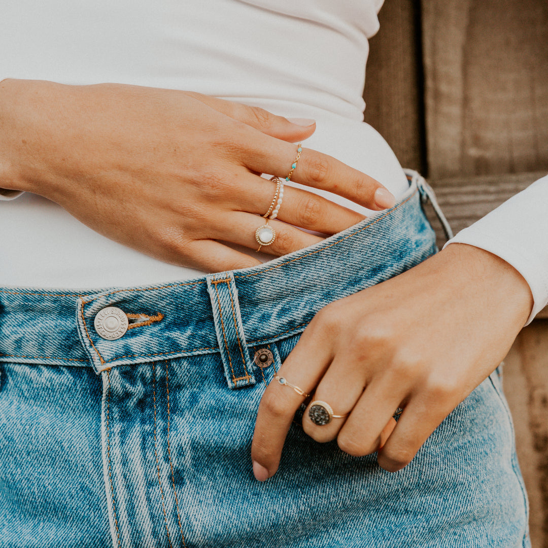 Close-up of hands wearing mother of pearl gemstone rings on a person wearing blue jeans.