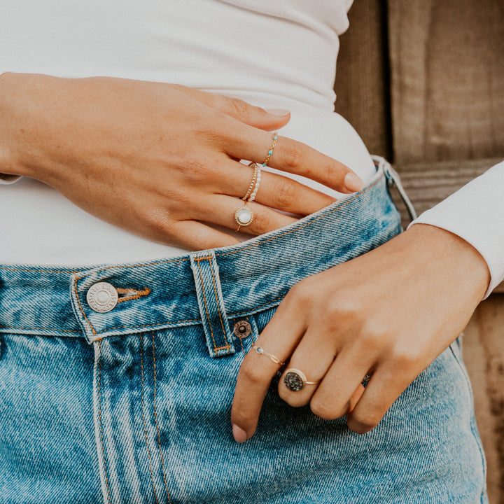 Close-up of hands wearing mother of pearl gemstone rings on a person wearing blue jeans.