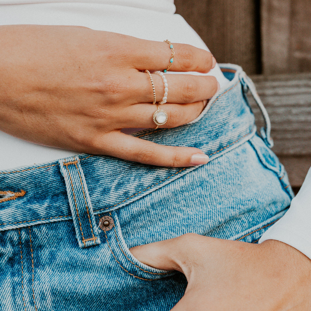  Close-up of hands wearing mother of pearl gemstone rings on a person wearing blue jeans.