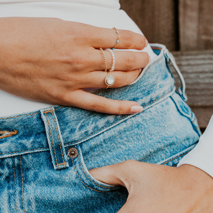  Close-up of hands wearing mother of pearl gemstone rings on a person wearing blue jeans.