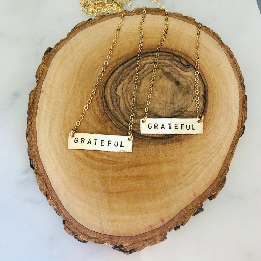 Teressa Lane Jewelry personalized bar necklace with grateful engraving on gold chain displayed on wooden slab