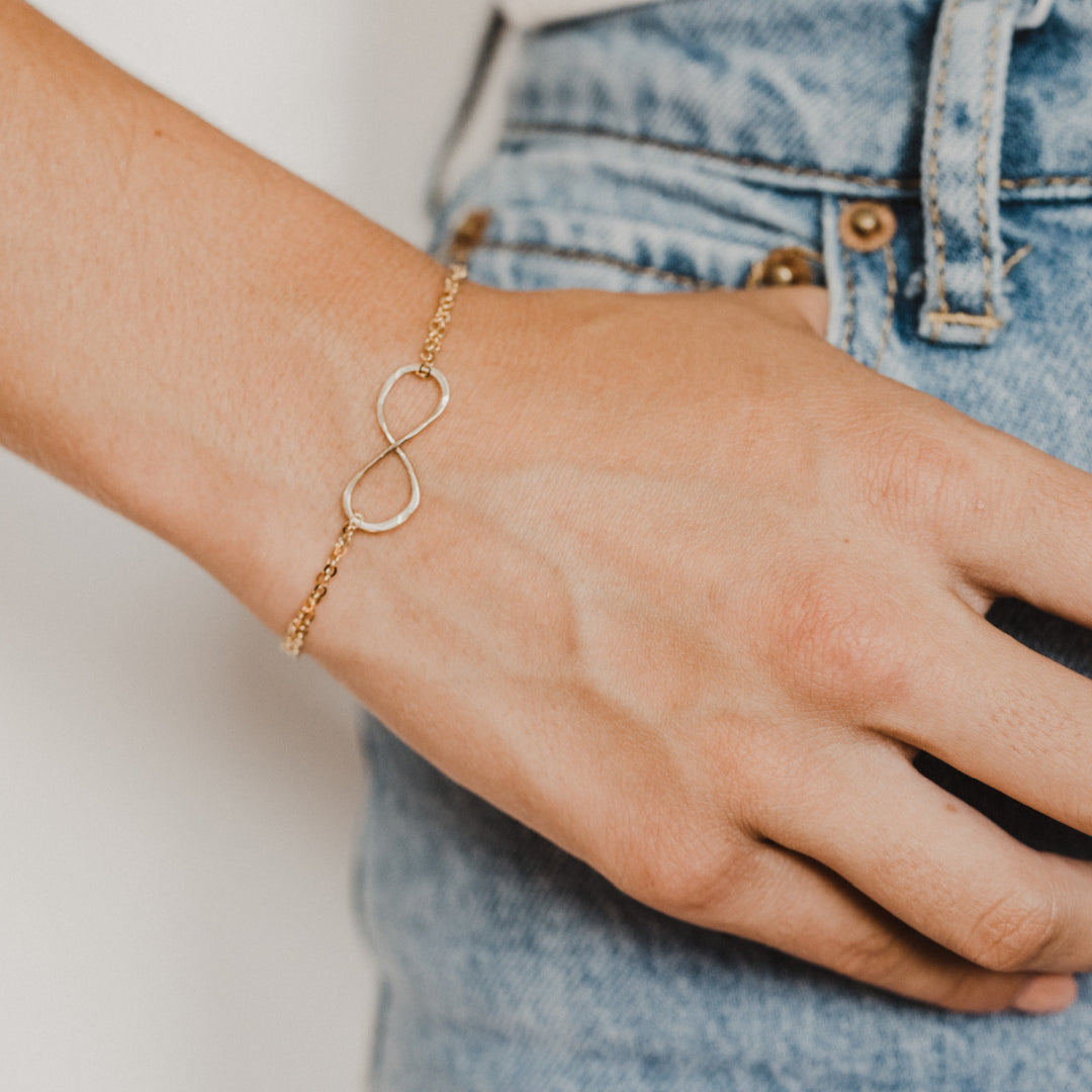 Teressa Lane Jewelry delicate gold infinity bracelet for women worn on wrist with denim jeans