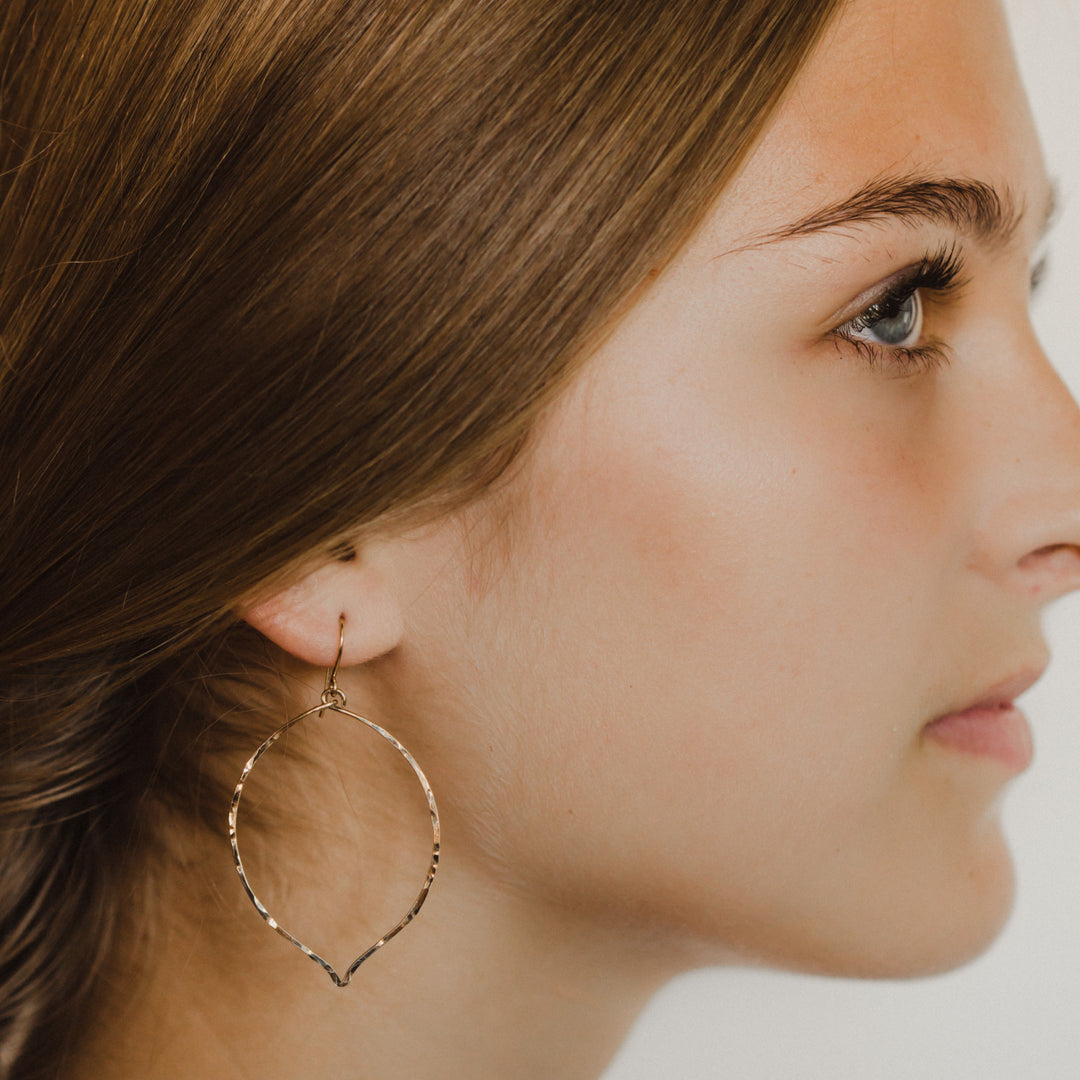 Close-up side view of woman wearing Teressa Lane Jewelry lotus dangle earrings in gold